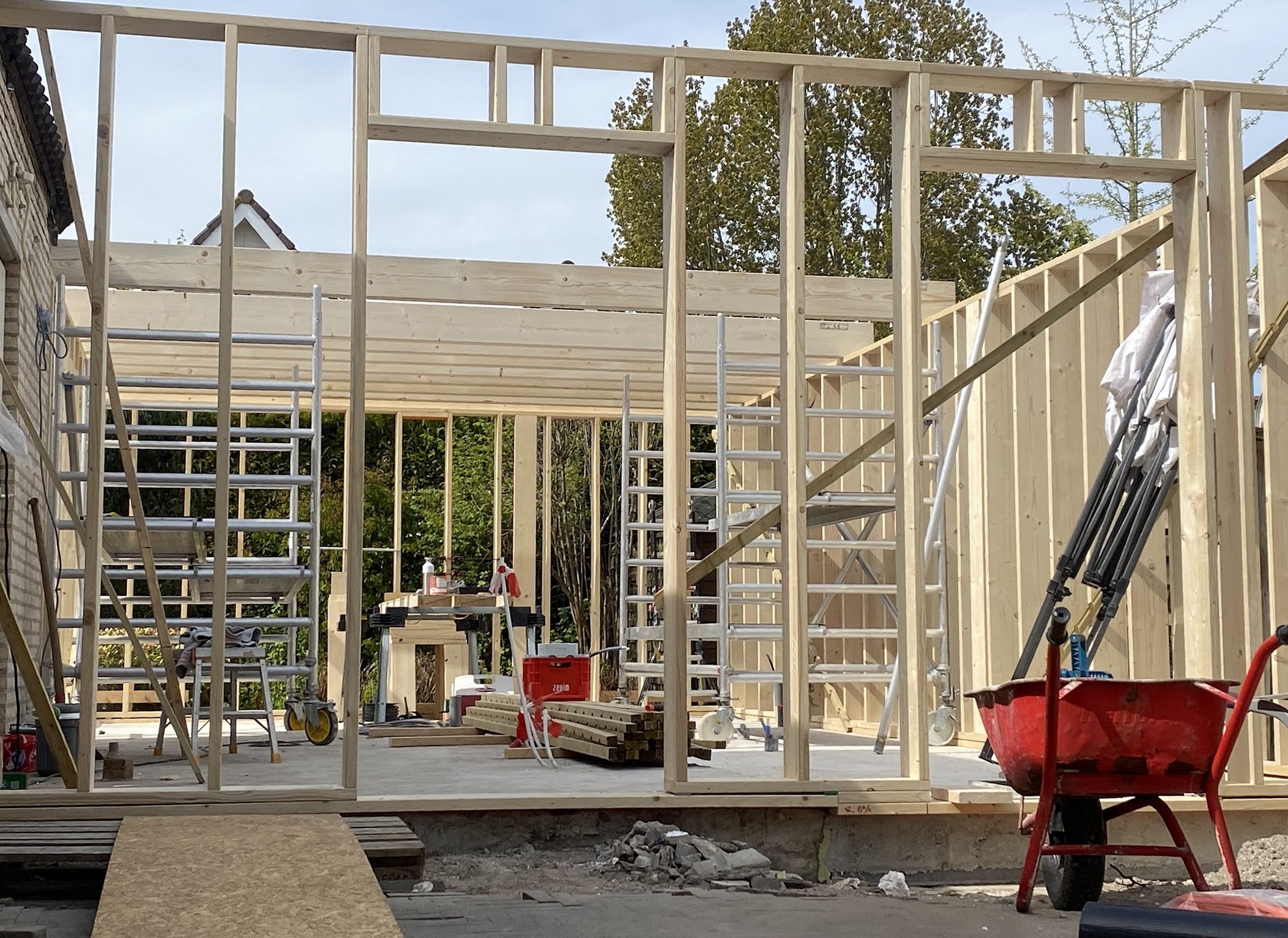 Houten frame van een uitbouw in aanbouw, stijlen en balken staan, steiger ernaast