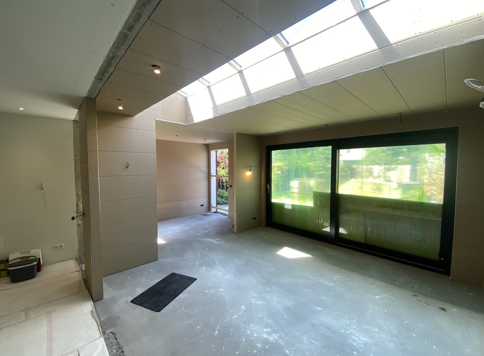 Uitbouw in afwerkfase met een lange lichtstraat in het plafond en een grote schuifpui naar de tuin