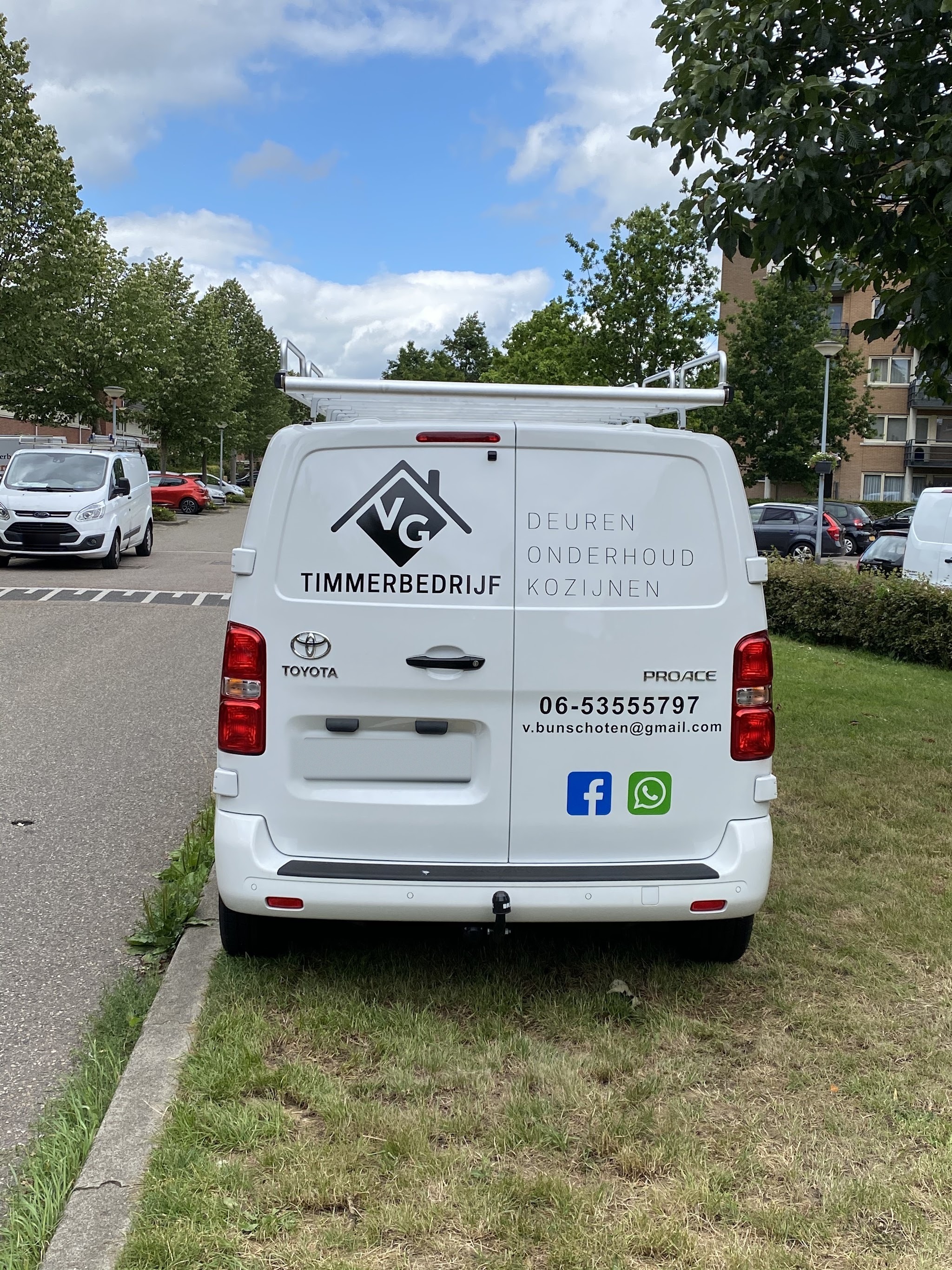 Achterkant van de witte bedrijfsbus met het VG-logo, de woorden deuren, onderhoud, kozijnen en het telefoonnummer